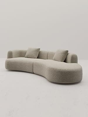 A large, modular, curved sofa with a textured, boucle-like upholstery. The sofa features rounded edges and appears to be composed of at least two connected sections, forming a sweeping arc. It includes two square throw pillows that match the sofa's upholstery. The design is contemporary with a soft, inviting aesthetic. — 3D model