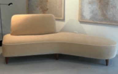 A modern asymmetrical chaise lounge upholstered in a light beige fabric with contrasting white piping, supported by tapered wooden legs. — 3D model