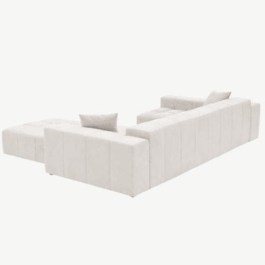 A contemporary sectional sofa with a tufted upholstery design. The sofa features a chaise lounge section extending from the main body. It is upholstered in a light cream-colored fabric with a soft texture. The design incorporates horizontal tufting on the seat and back cushions, creating a grid-like pattern. Two square throw pillows, matching the sofa's upholstery, are placed on the sofa. The sofa sits on low-profile, dark-colored feet. — 3D model