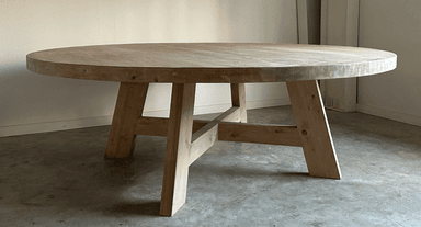 A round dining table with a thick, solid wood top and a substantial base constructed from heavy timber. The base features four angled legs connected by a cross-brace structure, providing stability and a rustic aesthetic. — 3D model