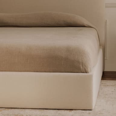A modern platform bed with a gently curved, upholstered headboard and a rectangular, upholstered base. The bed is dressed in neutral-toned linens. Flanking the bed are two matching wooden nightstands with minimalist designs, featuring drawers and open shelving. — 3D model