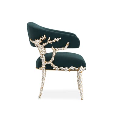 A luxurious barrel-back accent chair featuring a deeply curved back and seat upholstered in dark emerald green velvet. The chair is supported by four highly decorative legs and arm supports, rendered in a lustrous gold finish with intricate white sculptural details resembling leaf motifs or scales. — 3D model