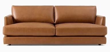 A contemporary two-seat loveseat upholstered in a warm, cognac-colored leather. It features a streamlined, low-profile design with plump, removable seat and back cushions. The armrests are subtly integrated, appearing as low, rounded track arms. The base is simple and rests on discreet, short feet, giving it a minimalist aesthetic. — 3D model