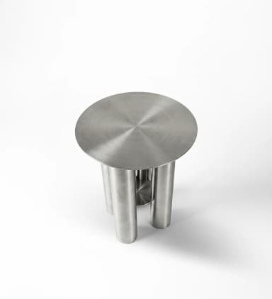 A small, round accent table constructed entirely from brushed stainless steel. It features a circular top supported by three large, cylindrical legs. One of the legs appears to be composed of two half-cylinders or has a vertical cutout, revealing a smaller internal cylindrical element or a void, adding a distinctive design element. The overall aesthetic is minimalist, modern, and industrial. — 3D model