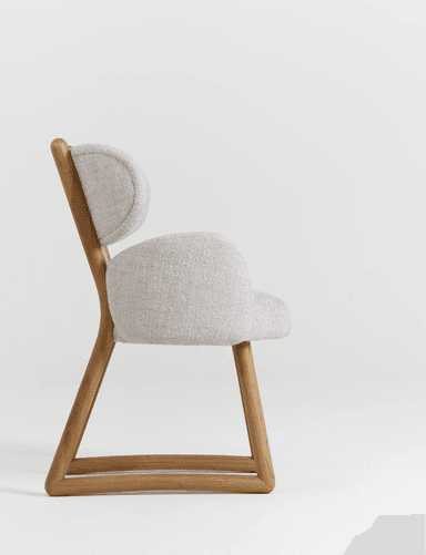 A modern armchair with a light grey upholstered seat, backrest, and armrests, supported by a natural wood frame. The frame has a distinctive angular design, particularly at the legs and where the backrest is supported. The upholstery has a textured fabric weave. — 3D model