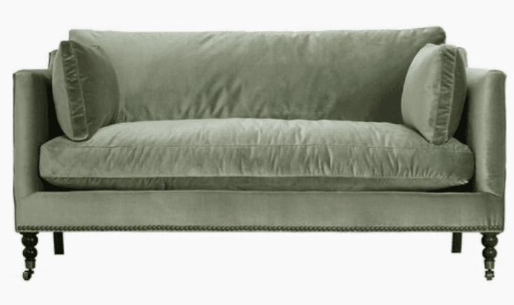 A contemporary two-seater sofa featuring a clean-lined silhouette, track arms, and plush cushioning. Upholstered in a soft, light green velvet or similar fabric, it includes two loose back cushions and a single bench-style seat cushion. The base is adorned with decorative nailhead trim along the bottom edge, and it stands on dark turned wood legs, with the front legs equipped with metal casters. — 3D model