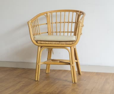 A natural-colored rattan armchair featuring a rounded backrest and integrated armrests, with a light cream-colored seat cushion. — 3D model