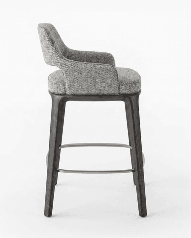 A modern bar stool with a fabric-upholstered seat and backrest, supported by dark-stained wooden legs. The stool features a curved back and armrests integrated into the main body. A metal footrest connects the four legs. — 3D model