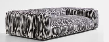 A contemporary two-seater sofa featuring a distinctive black and white zebra stripe pattern upholstery. The sofa has a boxy, low-profile silhouette with integrated armrests and backrest, presenting a seamless upholstered form without visible legs. Its design emphasizes comfort and a bold aesthetic statement. — 3D model