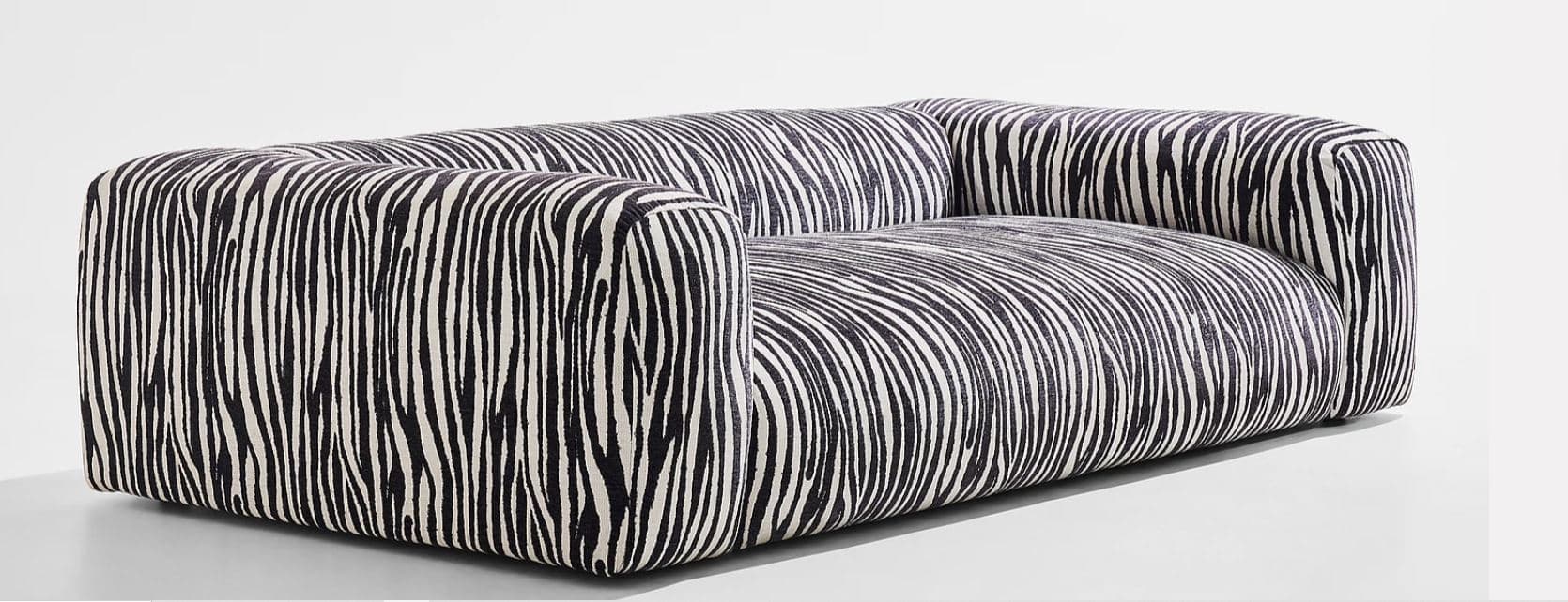 A contemporary two-seater sofa featuring a distinctive black and white zebra stripe pattern upholstery. The sofa has a boxy, low-profile silhouette with integrated armrests and backrest, presenting a seamless upholstered form without visible legs. Its design emphasizes comfort and a bold aesthetic statement. — 3D model
