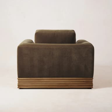 A single-seater armchair with a plush, upholstered body and a distinct wooden base. The armchair features a deep seat, substantial armrests, and a high back cushion. The base is constructed from horizontally oriented wooden slats with a textured finish, providing a contrast to the soft upholstery. — 3D model