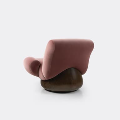 A contemporary lounge chair featuring a distinctive sculptural form. The upper body is upholstered in a plush, dusky pink velvet fabric, creating soft, organic curves that form the seat, backrest, and integrated armrests. This upholstered section rests upon a substantial, dark stained solid wood base that is round and bulbous, providing stability and a swivel function. The chair has a low profile and an inviting, enveloping design. — 3D model