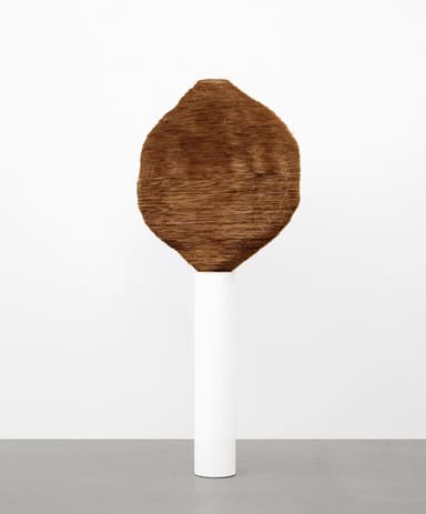 A large, irregularly shaped abstract sculpture with a textured, woven surface in a rich brown hue, displayed prominently on a tall, minimalist white cylindrical pedestal. — 3D model