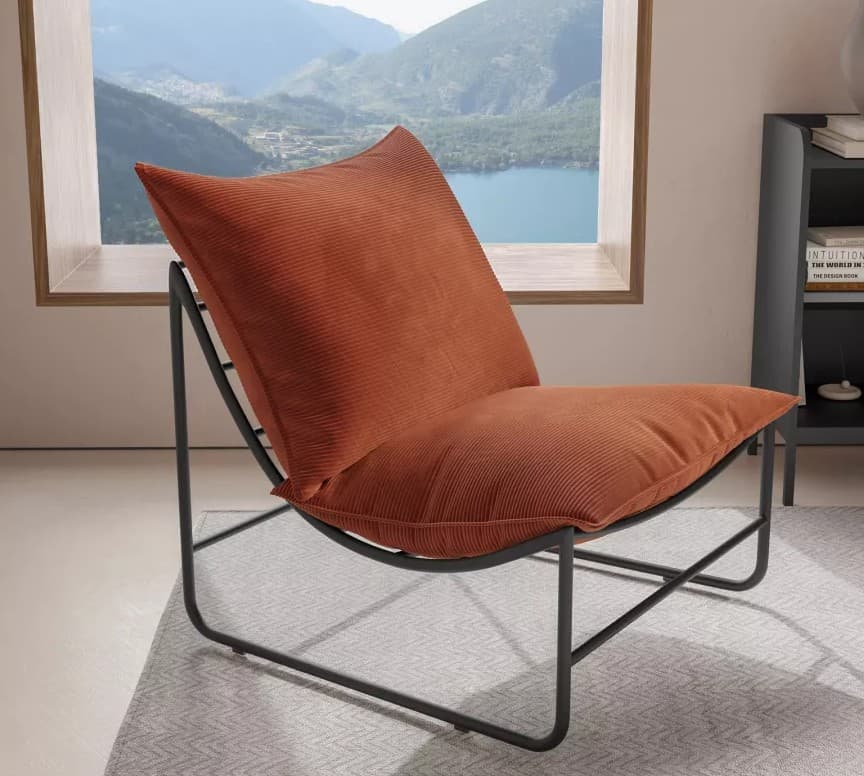 A contemporary armchair featuring a minimalistic black metal frame supporting a plush, corduroy-upholstered cushion in a warm terracotta or rust orange color. The frame has a fluid, curved design with intersecting linear elements for stability. The seat and backrest are integrated into a single, generously padded unit. — 3D model