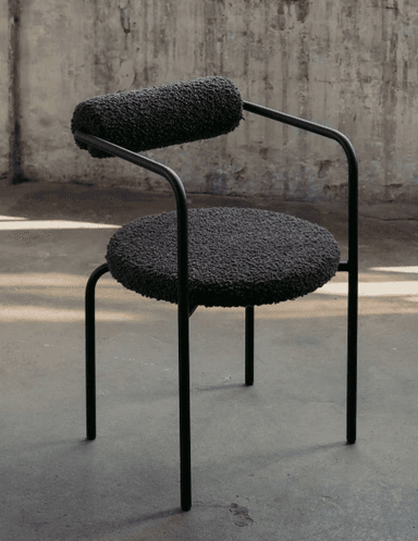 A modern chair with a rounded seat and a cylindrical backrest, both upholstered in a textured, dark gray fabric. The frame and legs are made of slender, black metal tubing. The armrests are formed by the continuous curve of the metal frame from the backrest to the front. — 3D model