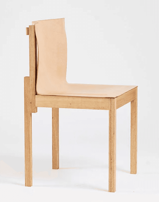 An armless chair featuring a light-toned oak wood frame and a single piece of natural saddle leather forming both the seat and the backrest. The design is minimalist with clean lines and visible wood grain. — 3D model