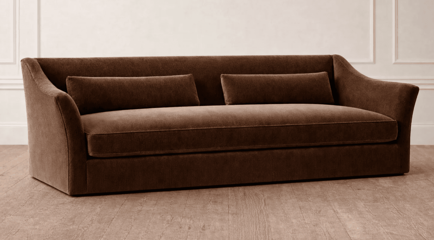 A contemporary three-seater sofa upholstered in a rich brown fabric, featuring a single, long bench cushion for seating. The backrest is gently sloped, flowing into slightly outward-curving, low-profile armrests. Two matching cylindrical bolster pillows are placed against the backrest. The sofa has a clean, minimalist base, suggesting a low-profile design without visible legs. — 3D model