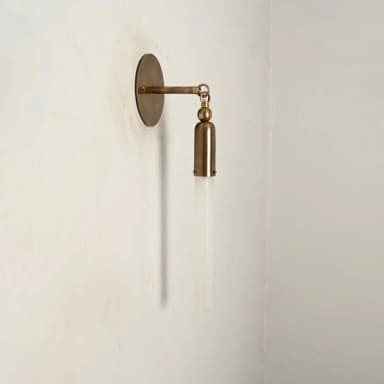 A modern wall sconce featuring a circular brass wall plate, an articulating arm, and a cylindrical brass housing holding a frosted glass rod-shaped shade. — 3D model