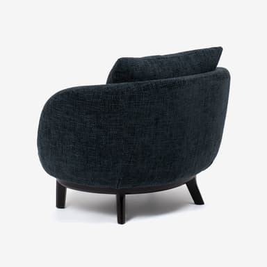 A modern armchair with a rounded, enveloping silhouette. The chair features a deep seat, a low-profile backrest, and integrated armrests that flow seamlessly into the body of the chair. A separate square cushion is placed against the backrest for added comfort. The chair is upholstered in a textured dark blue or charcoal fabric and rests on a dark, possibly wooden or metal, base with four short, tapered legs. — 3D model