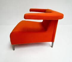A modern armchair with an asymmetric design. It features a curved seat and back, with one armrest extending outwards and upwards from the main body, while the other side is open. The chair is supported by four slender, cylindrical metal legs. — 3D model