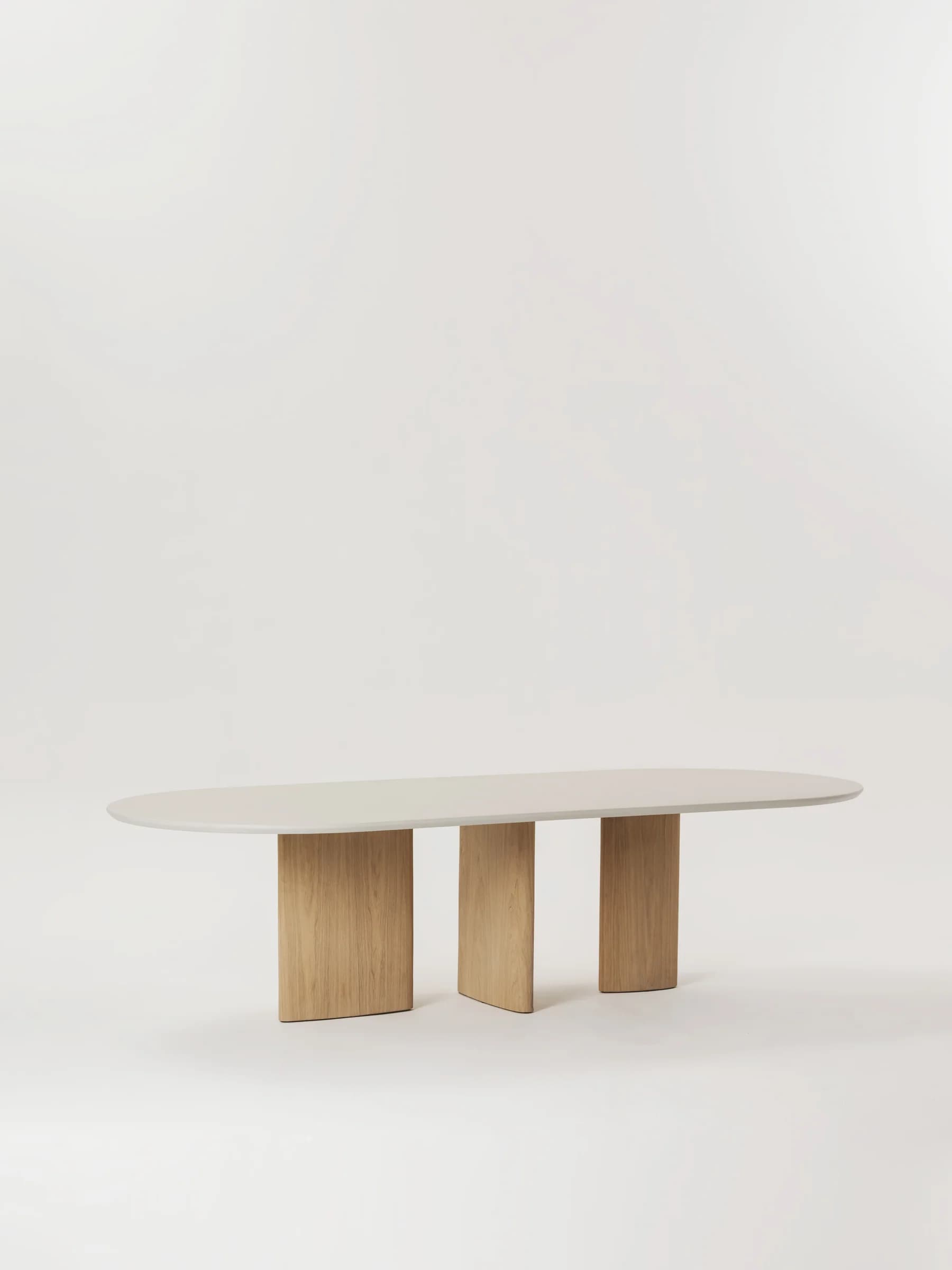 An oval-shaped dining table featuring a smooth, light grey tabletop and three substantial, solid wooden pillar bases. The design is contemporary and minimalist, emphasizing clean lines and natural materials. — 3D model