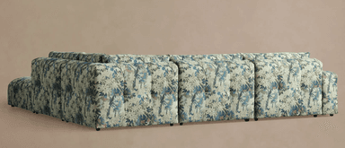 A sectional sofa with a corner chaise lounge. The sofa features a densely patterned upholstery with a botanical motif in shades of blue, green, and beige. It has a low profile with visible dark feet. — 3D model
