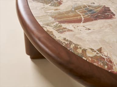 A low, round coffee table featuring a light-colored natural stone top, likely travertine, set within a thick, rounded frame of dark wood. The table is supported by four robust, chunky cylindrical wooden legs. — 3D model