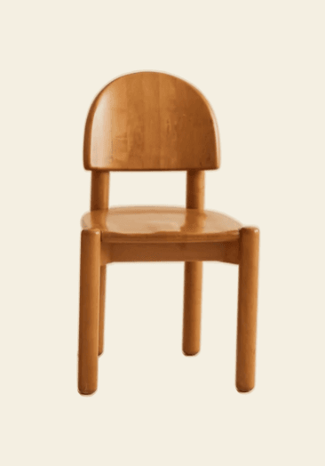 A small, light-toned wooden chair, likely for a child, featuring a minimalist design with rounded edges. The chair has a solid, curved backrest and a flat seat, supported by four thick, cylindrical legs. — 3D model