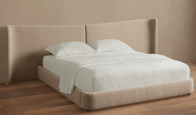 A contemporary upholstered platform bed featuring a distinctive winged headboard. The entire frame, including the headboard and bed base, is covered in a light beige, textured fabric. The headboard has a central seam and gracefully curved, outward-flaring wings on either side, providing a soft, enveloping aesthetic. The bed sits low to the ground on small, discreet feet. — 3D model
