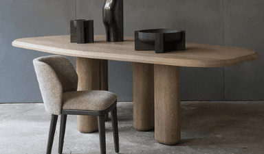 A contemporary dining table with a distinctive design featuring a smooth, dark wood tabletop and four cylindrical legs. The tabletop has rounded corners and a subtle curvature. The legs are thick and have a rounded profile, providing a sturdy base. A decorative black vase is placed on the table. — 3D model