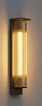 A tall, rectangular wall-mounted light fixture featuring a dark-toned metal backplate and a prominent fluted glass diffuser. The glass section is ribbed vertically and appears to be illuminated from within, casting a warm glow. The top of the metal frame and glass diffuser show an angular, stepped design, giving it a distinct Art Deco or classic modern aesthetic. The light is shown mounted on a textured, light-colored wall. — 3D model