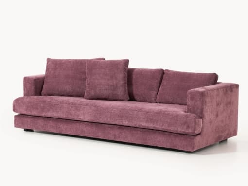 A three-seater sofa with a low profile and plush upholstery. It features wide armrests and a deep seat, complemented by four throw pillows. The base is slightly raised on dark, blocky feet. — 3D model