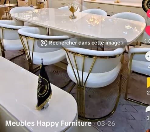A contemporary dining set featuring a white rectangular table with rounded corners and a gold-finished pedestal base, accompanied by six matching dining chairs. Each chair has a white upholstered seat and backrest, supported by an intricate gold-finished metal wireframe base and back structure. — 3D model