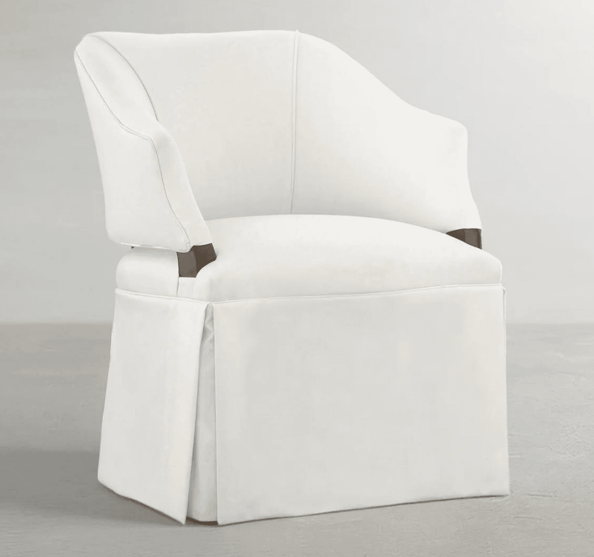 A fully upholstered armchair featuring a clean, off-white fabric and a skirted base that conceals the legs. The chair has a gently curved backrest and armrests that are integrated into the frame, with subtle exposed dark wood accents visible where the armrests meet the seat. The skirt is pleated at the corners, providing a tailored and classic appearance. The overall design is elegant and transitional, suitable for various interior styles. — 3D model