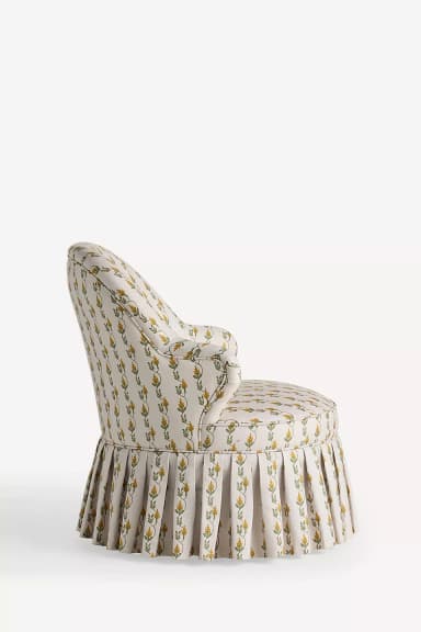 An upholstered armchair with a rounded back, rolled arms, and a pleated skirted base, covered in a cream fabric with a yellow and green botanical pattern. — 3D model
