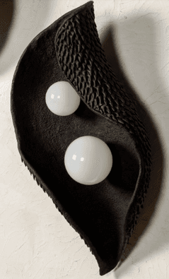 A sculptural wall sconce featuring a dark, leaf-like or organic-shaped body with a distinct textured surface. Two spherical, opaline white diffusers are embedded within the body, providing soft, diffused illumination. The fixture is designed for wall mounting and presents a modern, artistic aesthetic. — 3D model