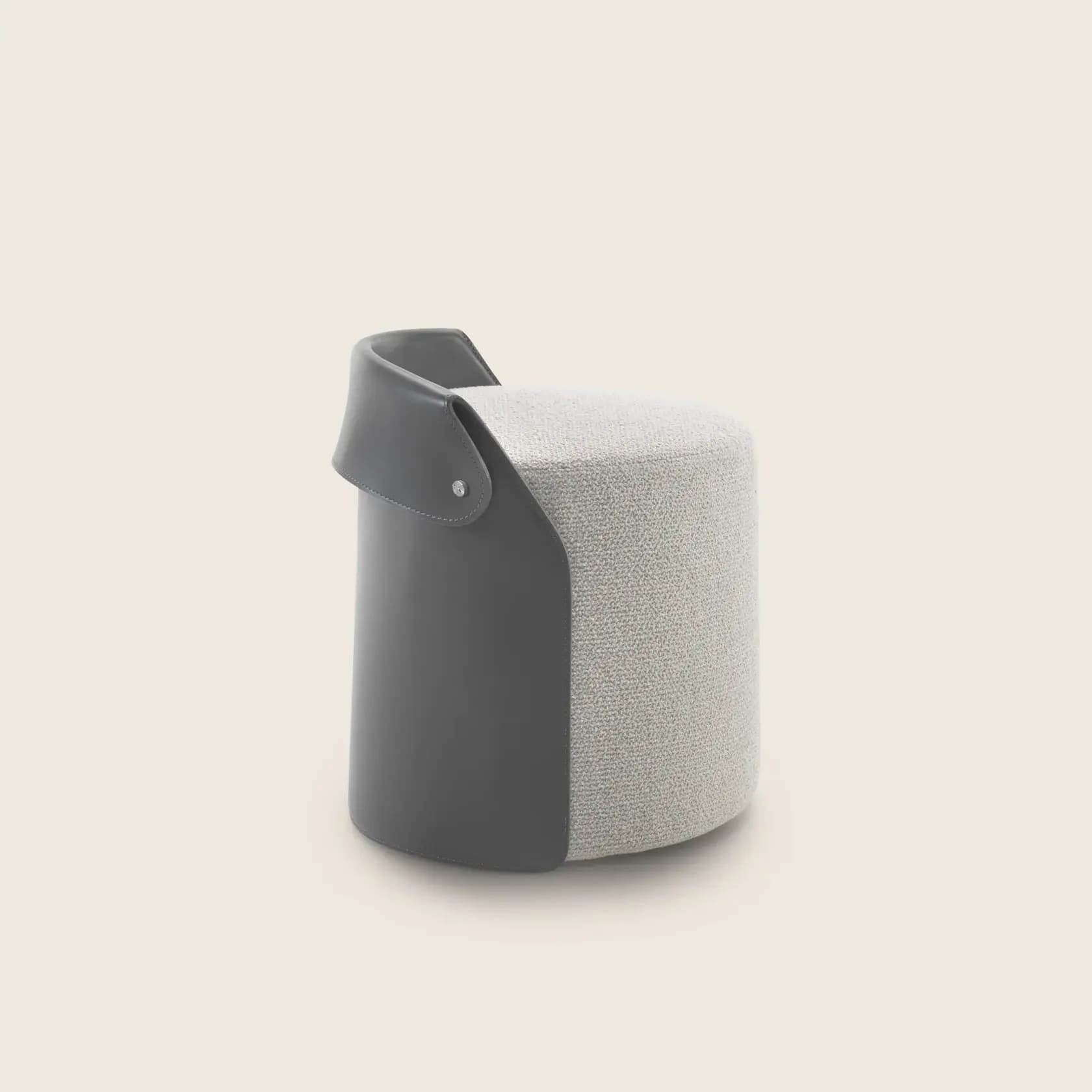A compact, cylindrical stool featuring a two-tone design. The main body is upholstered in a light grey, textured fabric, while a portion of the side is wrapped in a dark grey leather accent, secured by a single visible metal stud. The leather also forms a slightly raised lip or handle-like detail at the top edge. — 3D model