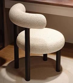 A modern armchair with a distinct curved backrest and a rounded seat. The upholstery is a textured boucle fabric, and the frame consists of dark, cylindrical legs and a supporting structure for the backrest. — 3D model