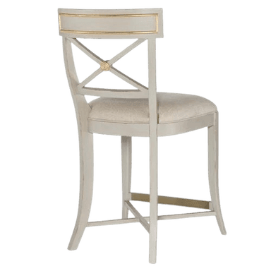 An elegant neoclassical-style counter stool featuring a light grey painted wooden frame with antique gold accents. The backrest has a distinct X-shaped splat with a central medallion, topped by a broad rail with gilded detailing. The seat is upholstered in a light cream fabric, providing comfort. The legs are tapered, and a golden metal footrest bar connects the front legs, while additional stretchers provide stability. — 3D model