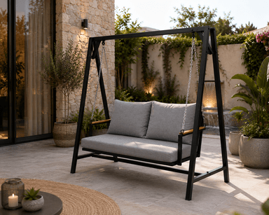 A contemporary freestanding two-seater swing bench featuring a black metal A-frame structure that supports a suspended seat. The seat is equipped with thick grey fabric cushions for both the backrest and the seat, and it has wooden accents on the armrests. The swing mechanism uses metal chains. — 3D model