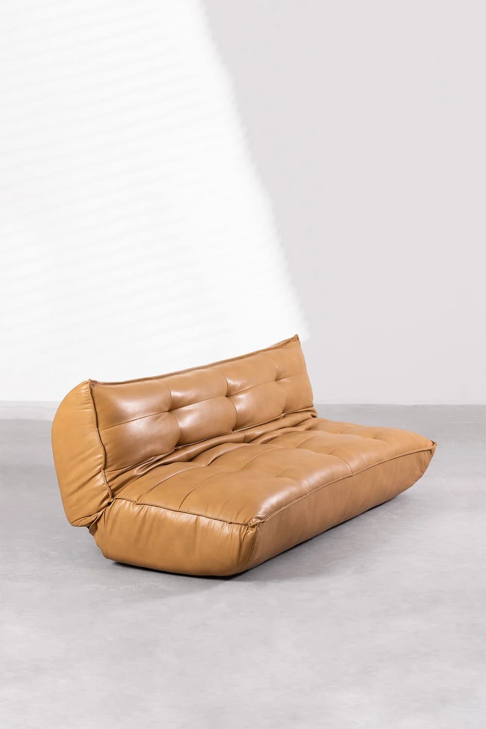 A low-profile, armless sofa with a tufted back and seat. The sofa features a rounded bolster-style armrest on the left side. Its design appears modern and casual, with soft, yielding cushioning. — 3D model