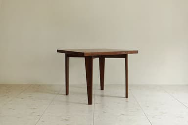 A square wooden table featuring a dark finish and four tapered legs, presented against a light-colored wall and tiled floor. — 3D model