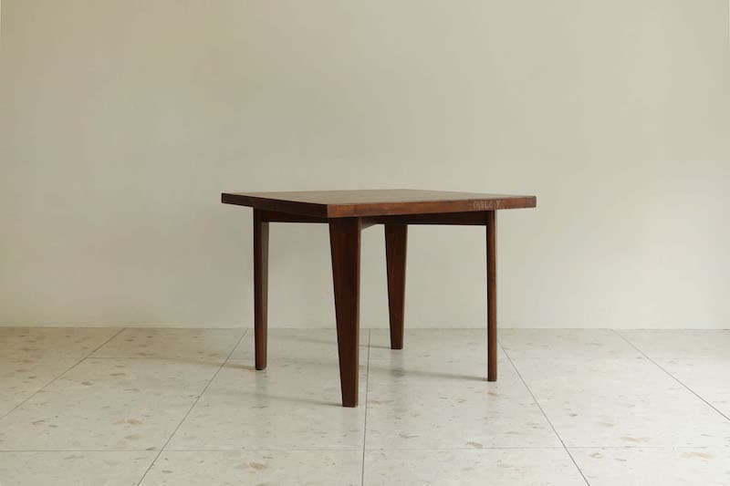 A square wooden table featuring a dark finish and four tapered legs, presented against a light-colored wall and tiled floor. — 3D model