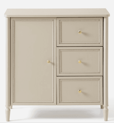 A compact, light beige storage unit featuring a cabinet door on the left and three stacked drawers on the right, all adorned with decorative beaded trim and brass knob hardware. It stands on four tapered, turned legs. — 3D model