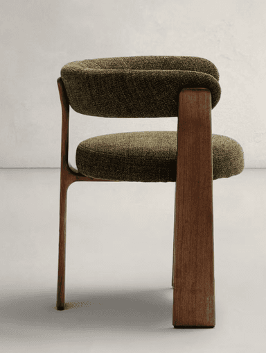 An armchair with a rounded, upholstered backrest and seat, supported by a solid wooden frame. The wooden elements have a visible grain and a matte finish, forming the legs and connecting the seat to the backrest. The upholstery is a textured fabric in a deep olive green color. — 3D model