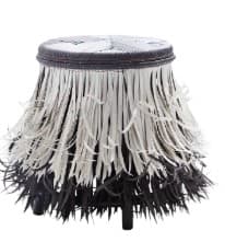 A round stool with a woven top and a decorative skirt made of alternating black and white fringe. The stool has a compact form and appears to be constructed from natural or synthetic fibers for the woven elements and possibly metal for the base and legs, which are not clearly visible but are suggested by the structure supporting the fringe. — 3D model