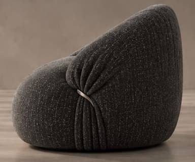 A contemporary, generously padded armchair with a sculptural and organic form, upholstered in a dark charcoal grey fabric with subtle white flecks. The chair features a rounded, low-slung profile and distinct pleating or gathering of the fabric, particularly evident around the armrests and base, giving it a plush, cloud-like appearance. A single, sleek silver-toned metal ring acts as a decorative and structural detail on one side, cinching the upholstery. — 3D model