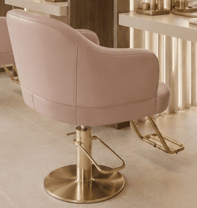 A modern hydraulic salon stylist chair featuring a plush, light pink upholstered seat and back, complemented by a polished gold circular base and an integrated gold-finished footrest. The chair includes curved armrests and a hydraulic lift mechanism for height adjustment. — 3D model