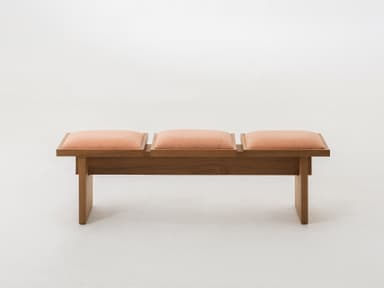A modern bench crafted from light-toned oak wood, featuring a minimalist design. The bench is equipped with three individual, rectangular upholstered cushions in a textured peach-colored fabric, set within the wooden frame. The frame consists of a sturdy base and two plank-style legs. — 3D model