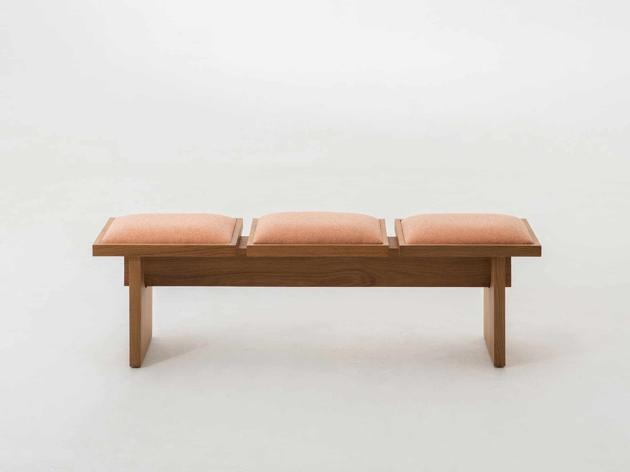 A modern bench crafted from light-toned oak wood, featuring a minimalist design. The bench is equipped with three individual, rectangular upholstered cushions in a textured peach-colored fabric, set within the wooden frame. The frame consists of a sturdy base and two plank-style legs. — 3D model